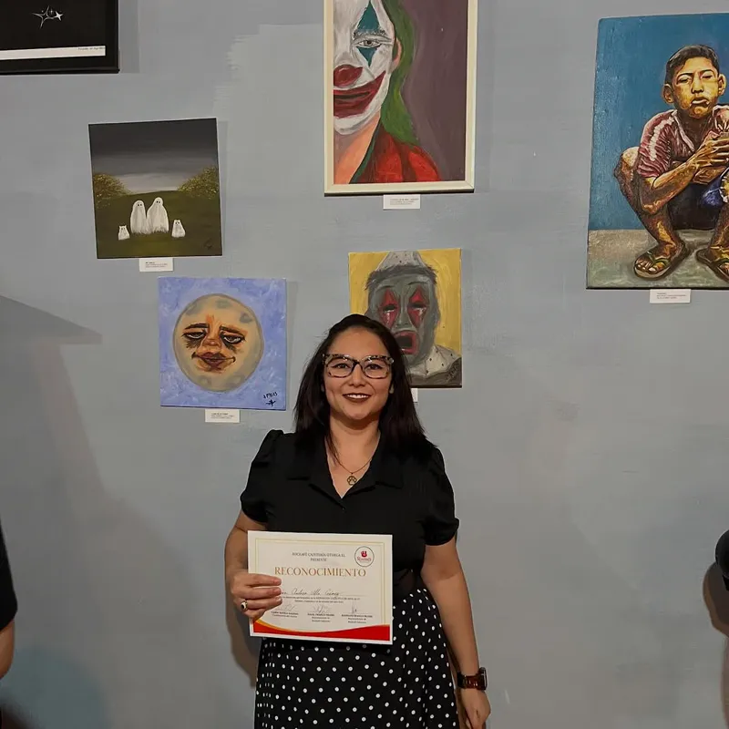 Sara Villa con su reconocimiento frente a sus pinturas en el Rockafé