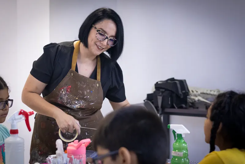 Sara Villa, con un rollo de cinta de papel en la mano, platica con los participantes sentados a la mesa