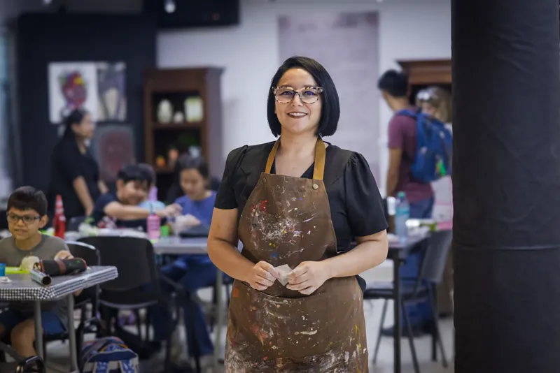 Sara Villa de pie en el salón de talleres; al fondo, mesas de trabajo y piezas en proceso