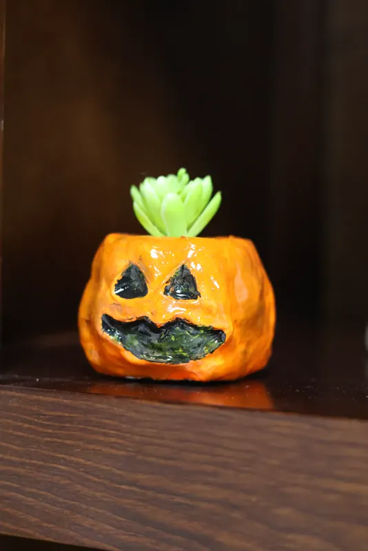 Ser torcido de arcilla: calabaza naranja con cara y un brote verde, en una vitrina de madera