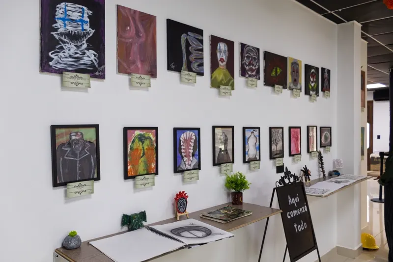 Muro con dos filas de pinturas con sus fichas, entre ellas Parálisis del sueño, Drácula y Área COVID; abajo, repisas con cuadernos de dibujo y piezas de arcilla