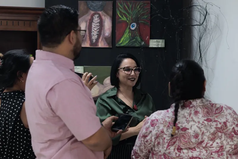 Sara Villa conversa con reporteros de espaldas a la cámara, frente a sus pinturas