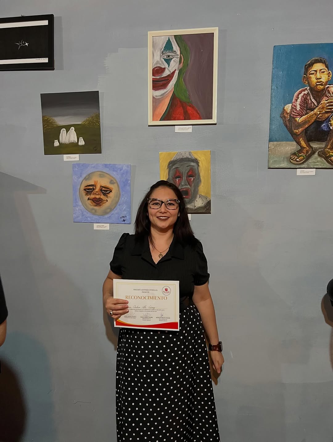 Sara Villa sostiene su reconocimiento frente a sus pinturas colgadas en la pared del Rockafé