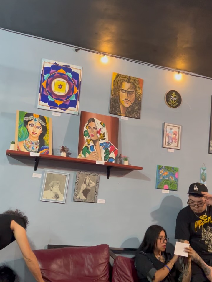 Pared del Rockafé con las obras de los artistas de la exposición colectiva y público sentado en los sillones